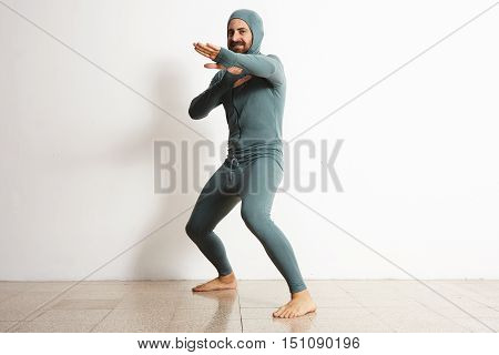Happy smiling bearded fitted male wearing snowboarding thermal baselayer suite from merino wool and acts like a ninja in defend position, isolated on white