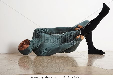 Funny fitted male athlete in winter thermal suite dressing up his long snowboard socks on floor , using all his power