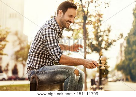 Young man is enjoying outside and playing by kendama.