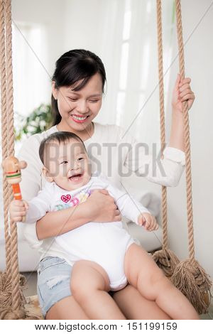 Portrait of happy asian mother and baby having fun together at home in white room near window