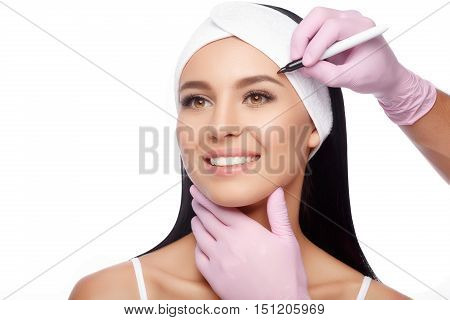 Young woman before plastic surgery operation. Beautiful woman ready for cosmetic surgery, female face with doctor's hands with pencil, over white. Woman face plastic operation. Aesthetic face