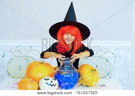 Little girl in witch costume during Halloween party playing around the table with pumpkins and bottle of potion