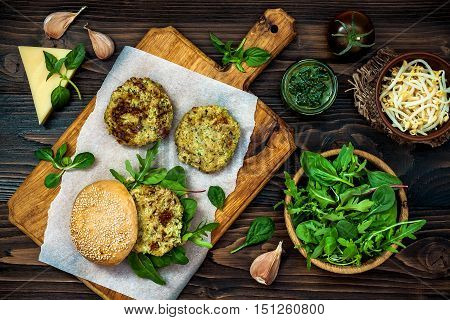 Zucchini quinoa veggie burger with pesto sauce and sprouts. Vegetarian burger on a cooking sheet ready to prepare hamburger. Top view overhead flat lay