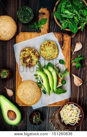 Zucchini quinoa veggie burger with pesto sauce and sprouts. Vegetarian burger on a cooking sheet ready to prepare hamburger. Top view overhead flat lay