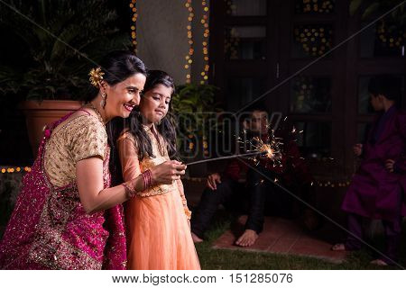 Indian mother and daughter playing with firecrackers or fire crackers or phuljhadi or fulzadi on diwali night