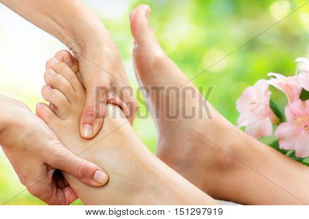 Macro close up of reflexologist doing massage on upper part of foot.Out of focus flowers in green background.