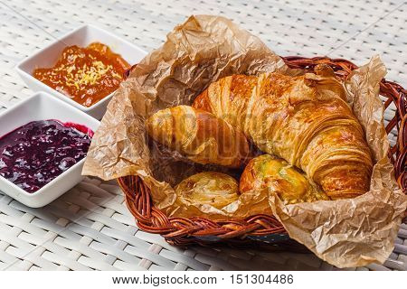 Croissants In Kraft Paper In A Breadbasket And Sweet Jam On The Table