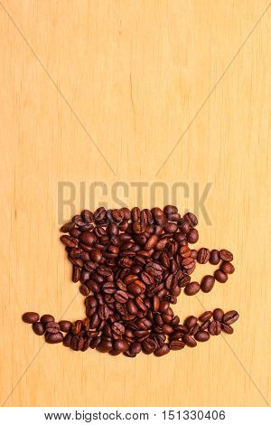 Roasted coffee beans placed in the shape of cup and saucer on wooden surface background copy space text area