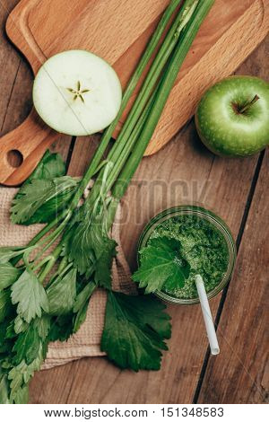 Overhead view of green smoothie with celery and apple on rusic wooden table