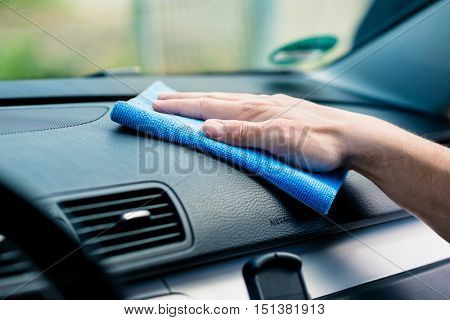 Man wiping the dashboard of his car with an anti-static cloth to remove accumulated dust, close up of his hand