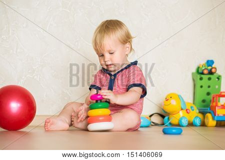 15 year-old child playing with educational cup toys at home. Little blond baby boy with blue eyes is playing with pyramid toy on the floor. Little kid have fun indoors