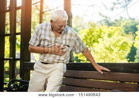 Senior man has heartache. Elderly guy near park bench. Pain is growing stronger. Pensioner needs medical attention.