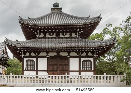 Kyoto Japan - September 15 2016: Smaller hall at Kurodani Buddhist Temple. Dark brown wood structure combines with snow white walls. Storm clouds and some green trees.