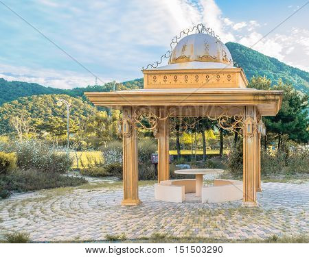 Landscape of a gazebo in a park with mountains, hills and a cloudy sky in the background