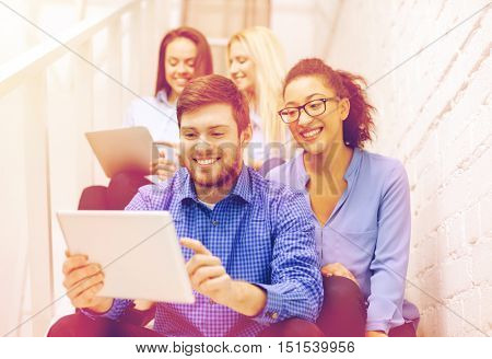 business, technology and startup concept - smiling creative team with tablet pc computer sitting on staircase