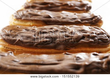 Delicious chocolate eclairs in row on white background, closeup