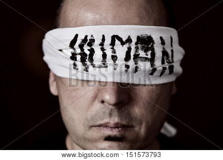 closeup of a young man with a blindfold in his eyes, with the word human handwritten in it