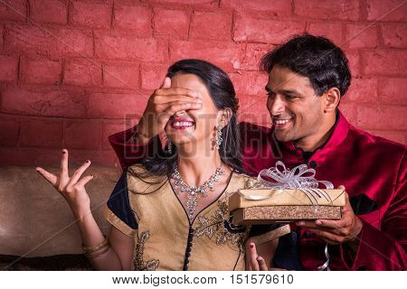 Indian husband surprising wife with a gift on diwali or anniversary or birthday, surprise gift concept and indian people or couple