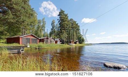 Group of red boathouse by the waterside pine trees and blue sky in the background