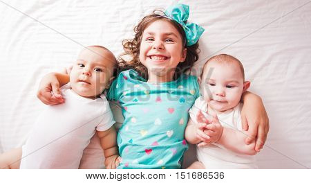 Five years old girl with her brothers - twins lying on the bed