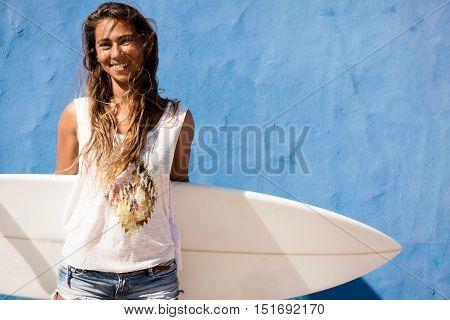 surfer girl with surfboard in front of blue wall