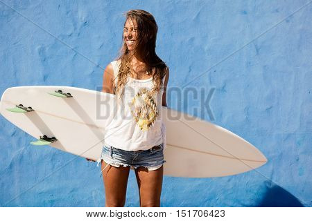 surfer girl with surfboard in front of blue wall
