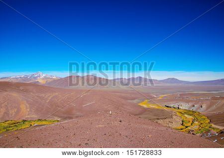 Panoramic view  over a green and yellow river between brown sandy hills on the way to Laguna Verde close to Copiapo in Chile, South America