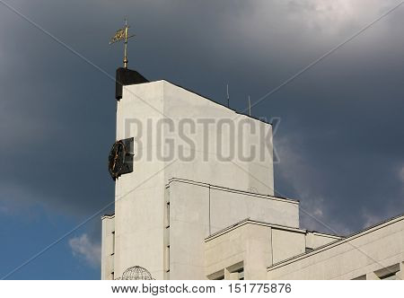Detail of a white building with a clock tower and the emblem of Belarus - Zubr - against the backdrop of a cloudy sky