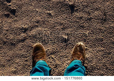 Male shoes on textured sand contrast blue trousers.