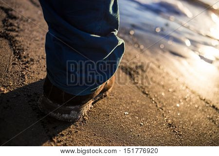 Male shoes on textured sea sand contrast blue trousers.