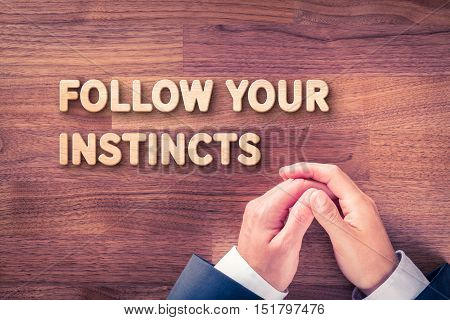 Follow your business instincts concept. Businessman and text Follow your instincts made from wood.