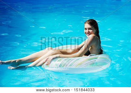 young sexy woman or girl with pretty face and wet hair swimming in pool on rubber ring with blue water sunny summer day outdoor