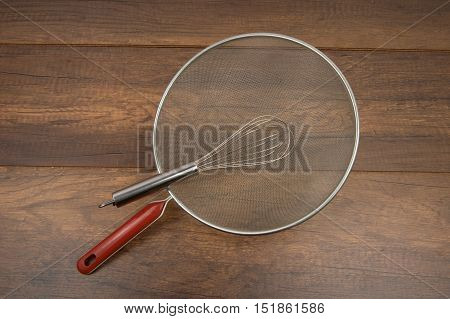 Metallic strainer with plastic handle and whisk on wooden background - a modern kitchen utensil.