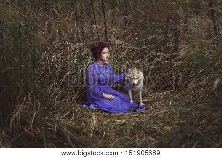 Woman sitting in tall grass next to the evil wolf they are friends.