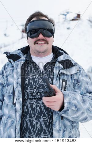 Half-length portrait of smiling man in black ski goggles holding radio standing outdoor.