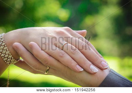 hands of Bridal couple with wedding rings on a green background