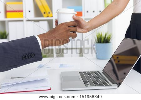 Close up of woman's hands giving paper cup of coffee to her coworker. Concept of office life and little acts of kindness