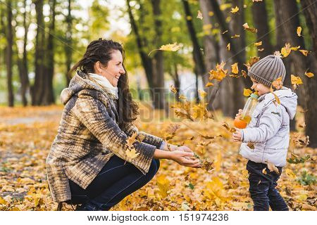 Adorable little boy with his mother in autumn park. Mother and son throws yellow leaves
