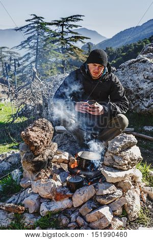 Wanderer cooking on bonfire, seating with hot cup of coffee. Turkey, Lycian way, touristic trail.