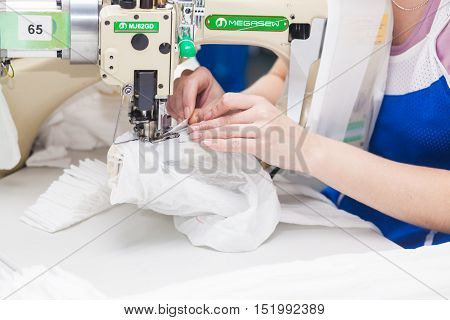 GRODNO BELARUS - DECEMBER 13 2013: Seamstress in textile factory sewing with a industrial sewing machine .