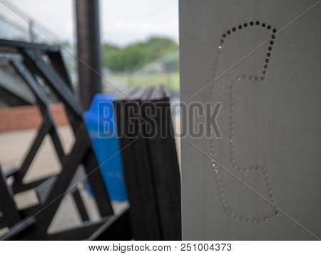 A Close Up Steel, Cutout Payphone Symbol In A Messy, Unmanaged Area