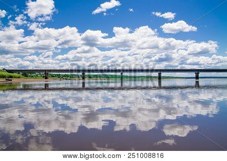 Steel Bridge With Lots Of Clouds In The Sky And Their Reflection In Water