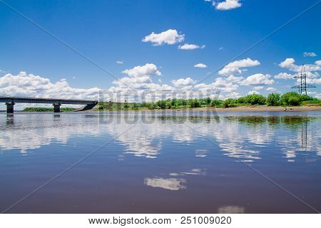 Steel Bridge With Lots Of Clouds In The Sky And Their Reflection In Water