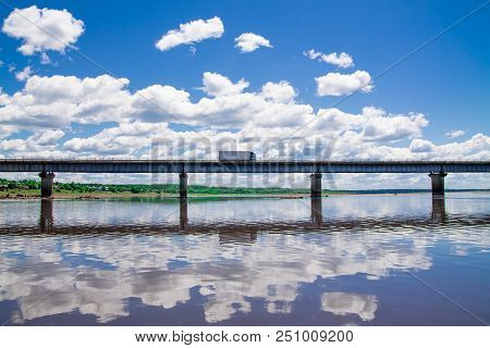 Steel Bridge With Lots Of Clouds In The Sky And Their Reflection In Water