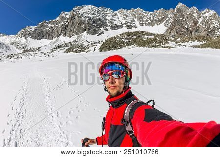 Selfi Male Mountaineer In Snowy Mountains, Wearing A Helmet With A Backpack.