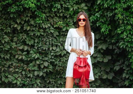 Close Up Image Of Happy Brunette Woman In Sunglasses And Red Bag Posing Sideways Outdoors