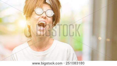 Crazy middle age woman wearing silly glasses stressful, terrified in panic, shouting exasperated and frustrated. Unpleasant gesture. Annoying work drives me crazy