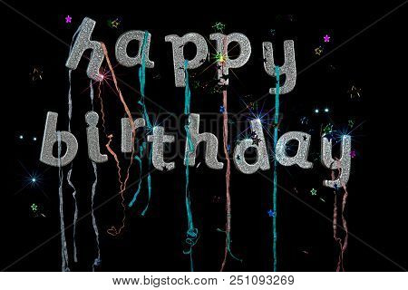 Happy Birthday. Greeting Card Text In Silver Glitter Letters With Streamers Stars And Fireworks Effe