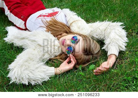 Fashion Hippie Young Girl Laying On Green Grass And Got Over Buuble Of Bubble Gum . Stylish Woman In