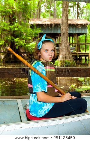 A Pre-teen Girl Sits In A Metal Canoe, Ready To Launch, With Paddle In Hand And A Smirk On Her Face.
